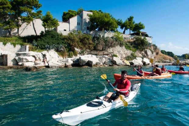A man kayaking on clear blue water near rocky cliffs and green trees