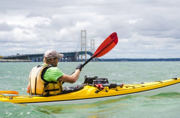 A man kayaking on green water with a large bridge in the background