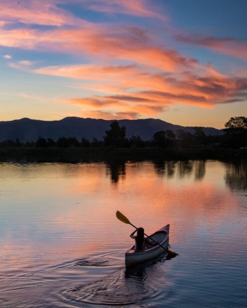 A person kayaking on a calm lake during a colorful sunset in the mountains