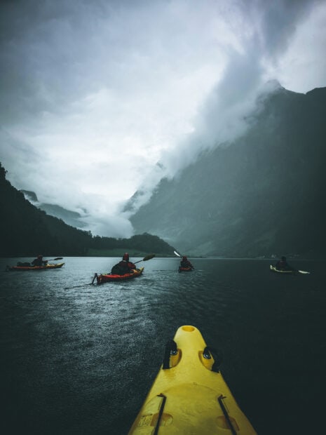 A group of kayaking enthusiasts paddling through a misty lake surrounded by towering mountains