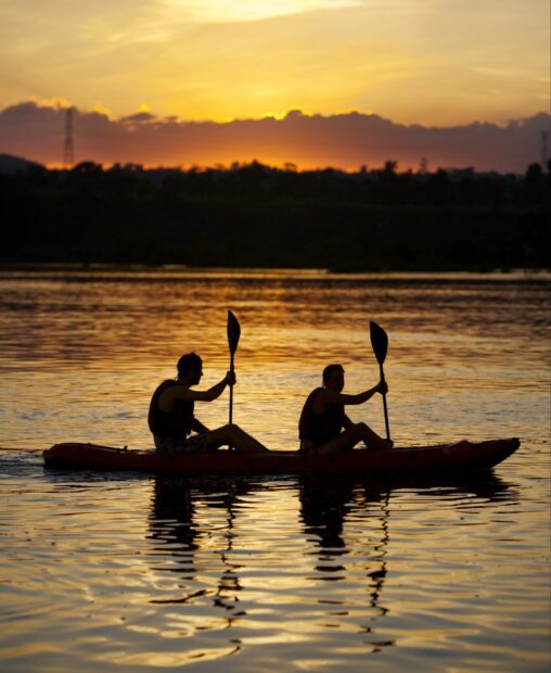 Two people kayaking on calm water during sunset with golden sky lighting