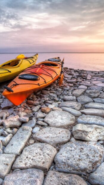 Orange and yellow kayaking boats resting on rocky shore at sunset