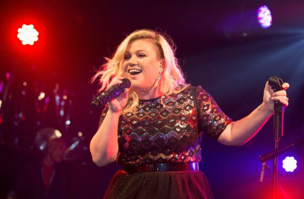 Kelly Clarkson singing on stage with a sparkling microphone in a black sequin outfit