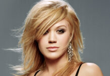 Kelly Clarkson portrait with blonde hair and chain earrings against a gray background