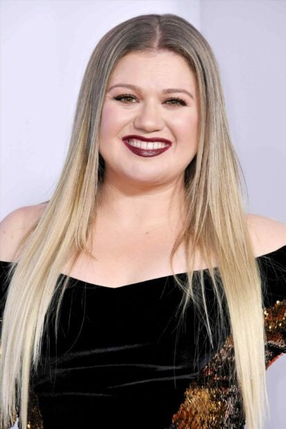 Kelly Clarkson with long blonde hair smiling in a black off shoulder dress