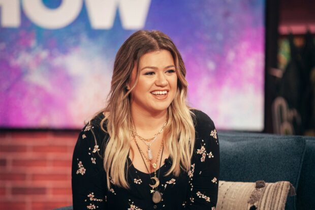 Kelly Clarkson smiling while sitting on a couch in a floral black dress