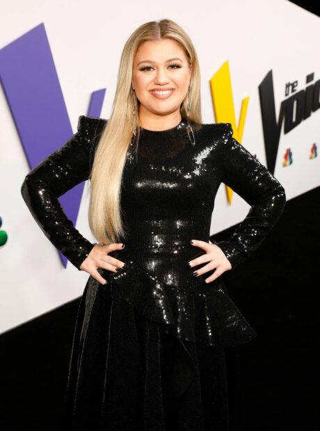 Kelly Clarkson wearing a black sequin dress smiling at the camera with hands on hips