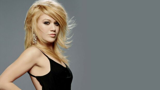 Kelly Clarkson posing confidently in a black dress with blonde hair and statement earrings