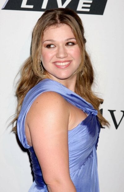 Kelly Clarkson wearing a blue dress smiling and looking to the side
