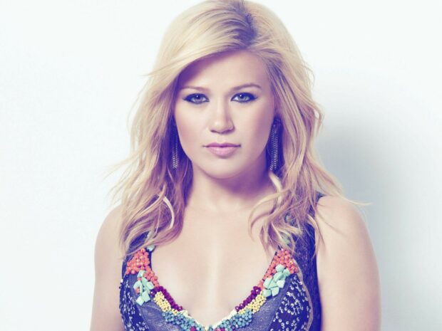 Kelly Clarkson wearing a colorful beaded top with blonde hair and blue eyes looking at the camera