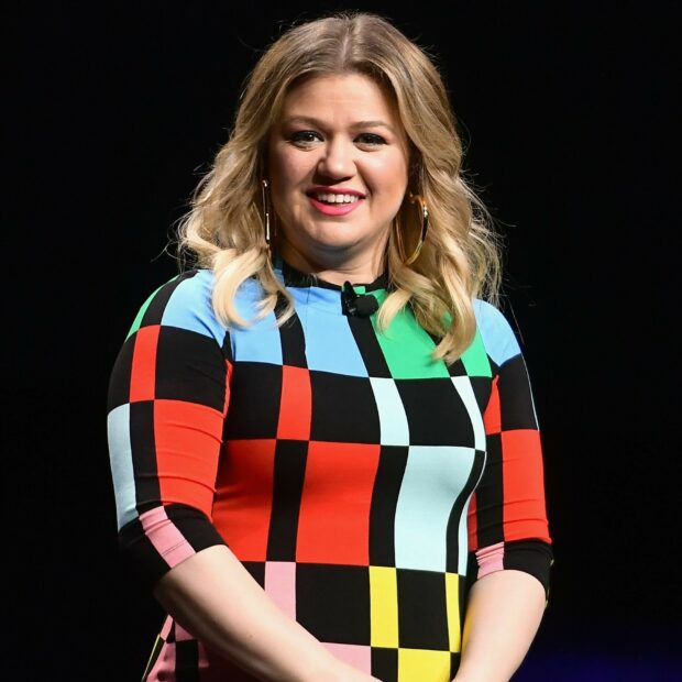 Kelly Clarkson wearing a colorful checkered dress smiling on stage