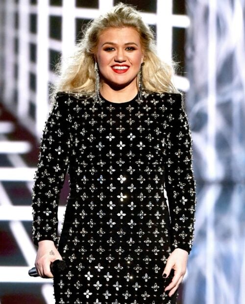 Kelly Clarkson wearing a black embellished dress smiling during a live performance