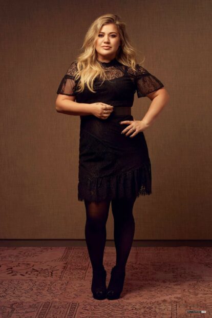 Kelly Clarkson wearing a black lace dress standing confidently in a studio setting