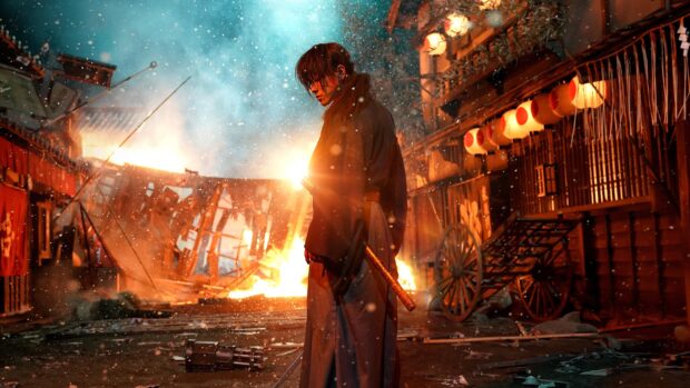 Kenshin standing in a burning street holding a sword in a dramatic scene with snow falling