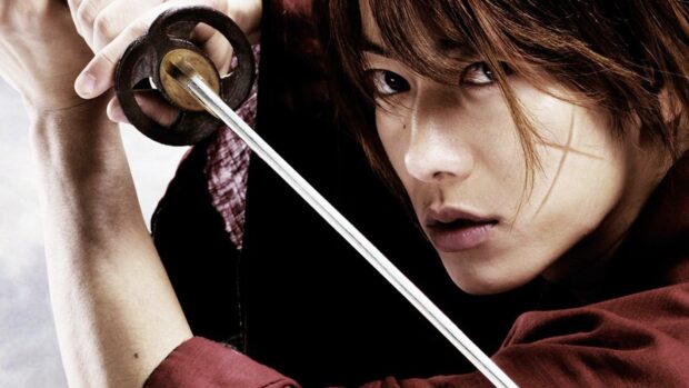 A close up of Kenshin holding a sword with a focused expression and a facial scar