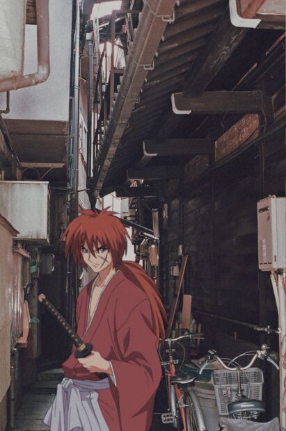 Kenshin standing with a sword in an old narrow alleyway in a traditional town