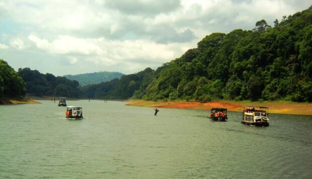 River with boats cruising through lush green Kerala forest landscape