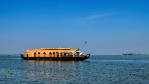 Traditional Kerala houseboat sailing on calm water under clear blue sky