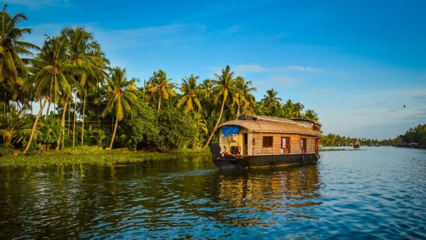 Traditional Kerala houseboat sailing on lush river surrounded by palm trees in Kerala