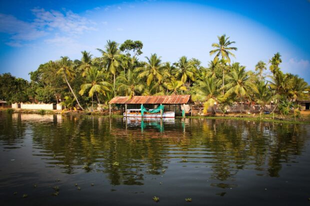 A serene Kerala river scene with palm trees and boats reflecting in the water