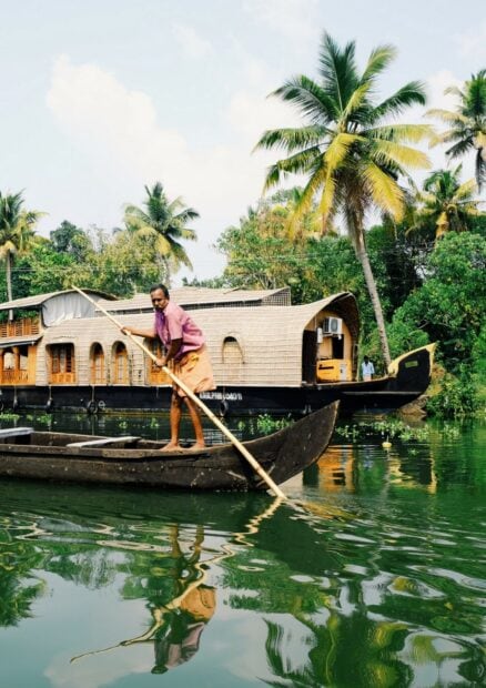 A man navigating a traditional boat in the calm waters of Kerala with lush palm trees in the background