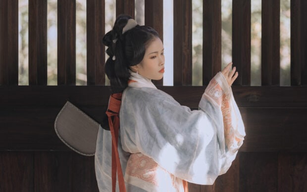 A woman wearing traditional kimono standing near wooden window with soft natural light