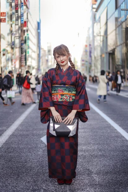 A woman wearing a checkered kimono standing in the middle of a city street