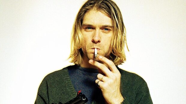 Kurt Cobain holding a cigarette and wearing rings with a green sweater