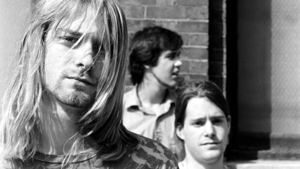 Kurt Cobain in a black and white portrait with two men in the background outdoors