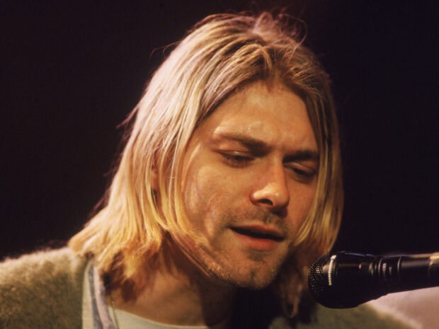 Kurt Cobain singing closely into a microphone with long blonde hair and focused expression