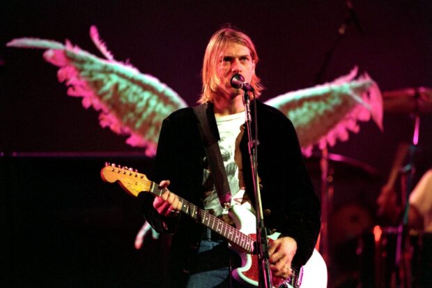Kurt Cobain playing guitar on stage with angel wings behind him