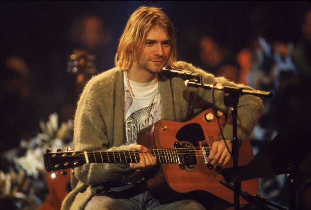Kurt Cobain playing acoustic guitar during a live performance in a cozy sweater