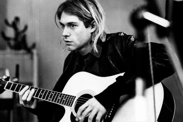 Kurt Cobain playing acoustic guitar in a black and white setting