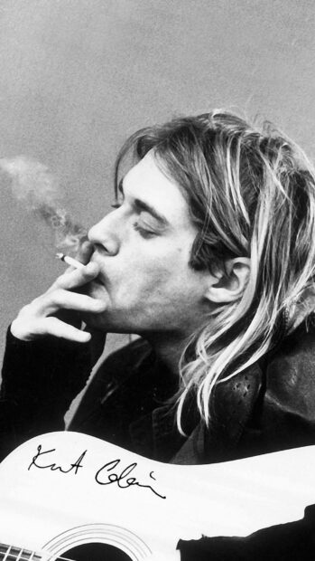Kurt Cobain smoking a cigarette while holding a guitar in a black and white portrait