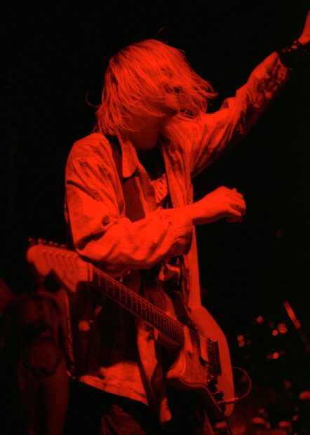 Kurt Cobain performing with his guitar under red lighting during a live concert