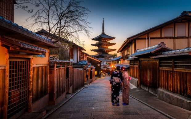 Two women wearing traditional kimonos walking in a historic Kyoto street near a pagoda at sunset