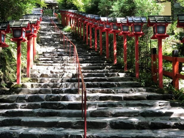 Stone stairs lined with red lanterns surrounded by lush greenery in Kyoto