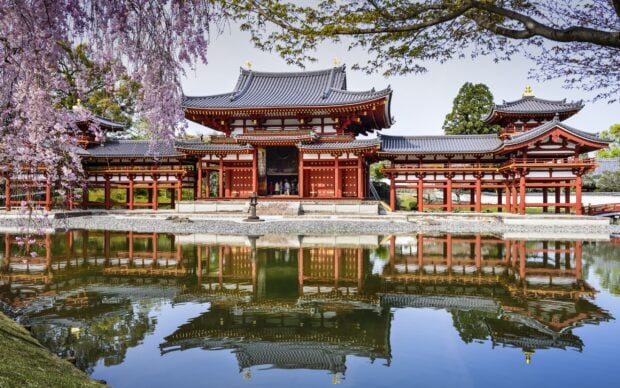 Traditional Kyoto architecture reflected in calm water with blooming cherry trees in spring