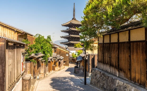 Traditional Kyoto street with wooden houses and pagoda in the background under clear sky