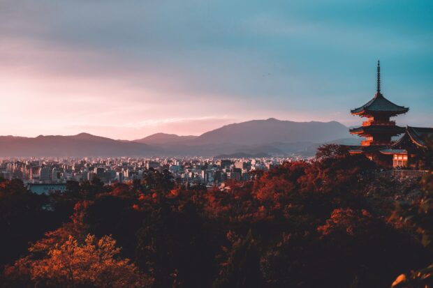 Traditional Kyoto temple surrounded by autumn trees with cityscape and mountains in the background