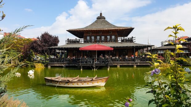 Traditional wooden architecture in Kyoto with a boat floating on green water and blooming flowers