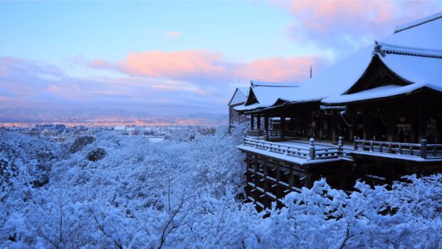 Snow covered temple and trees in Kyoto with city and mountains in the background
