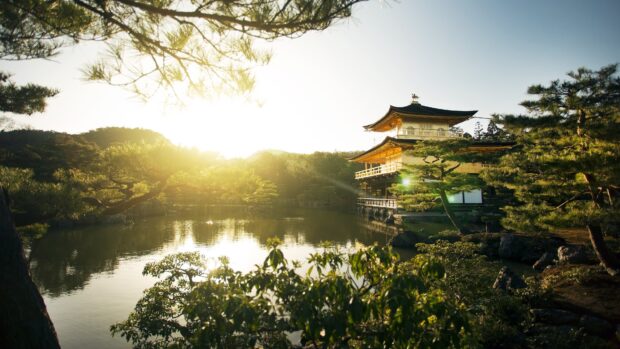 A golden pavilion surrounded by lush greenery near a calm lake in Kyoto at sunrise