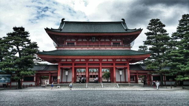 Traditional Kyoto architecture with red pillars and green roofs surrounded by trees and people