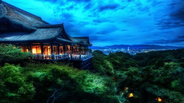 Traditional Kyoto building glowing at night surrounded by lush green trees and cityscape