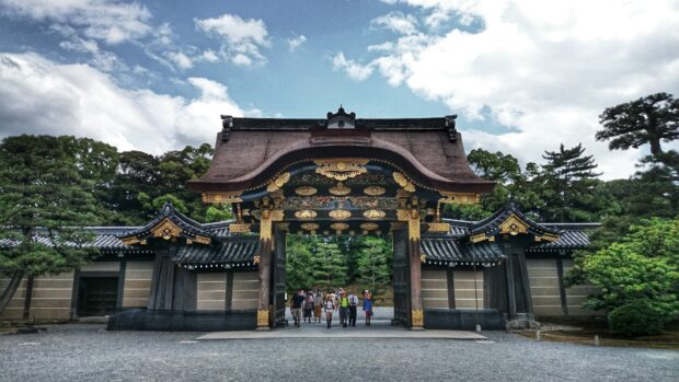 Traditional Kyoto gate with tourists walking under a decorated roof in a garden setting