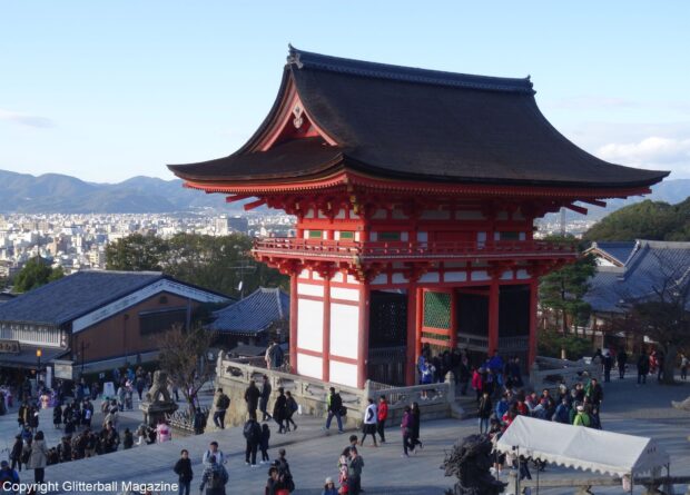 Traditional Kyoto architecture with a red temple gate and cityscape in the background