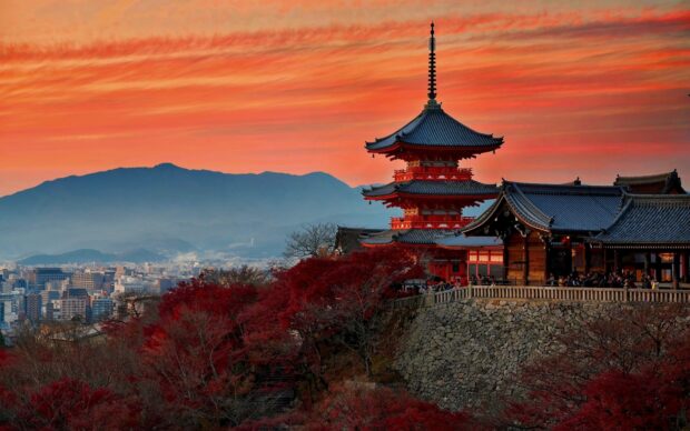 Traditional Kyoto pagoda surrounded by autumn trees under a colorful sunset sky