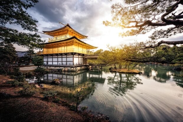 Golden pavilion in Kyoto surrounded by trees and a reflective pond during sunset