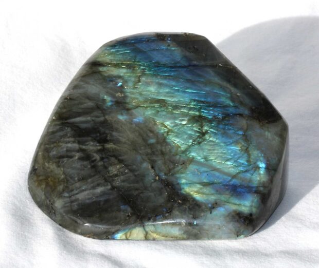 Polished labradorite stone showing vibrant blue and green reflections on a white surface